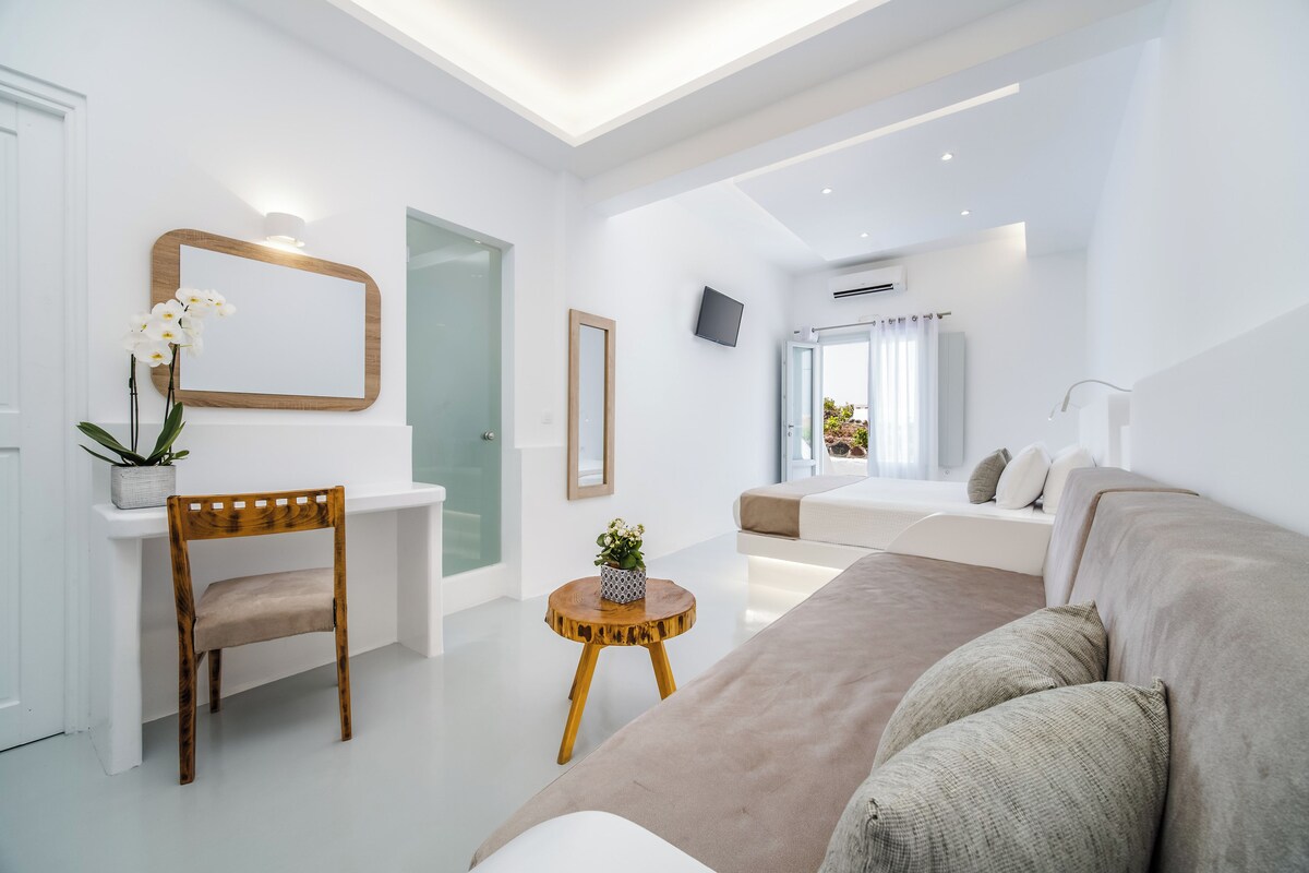 A modern living room with a sofa, a wooden chair, a small round table, and a mirror on the wall.