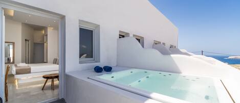 A modern, white infinity pool with a glass edge, a cozy seating area with a sofa and a small table, and a view of the ocean.