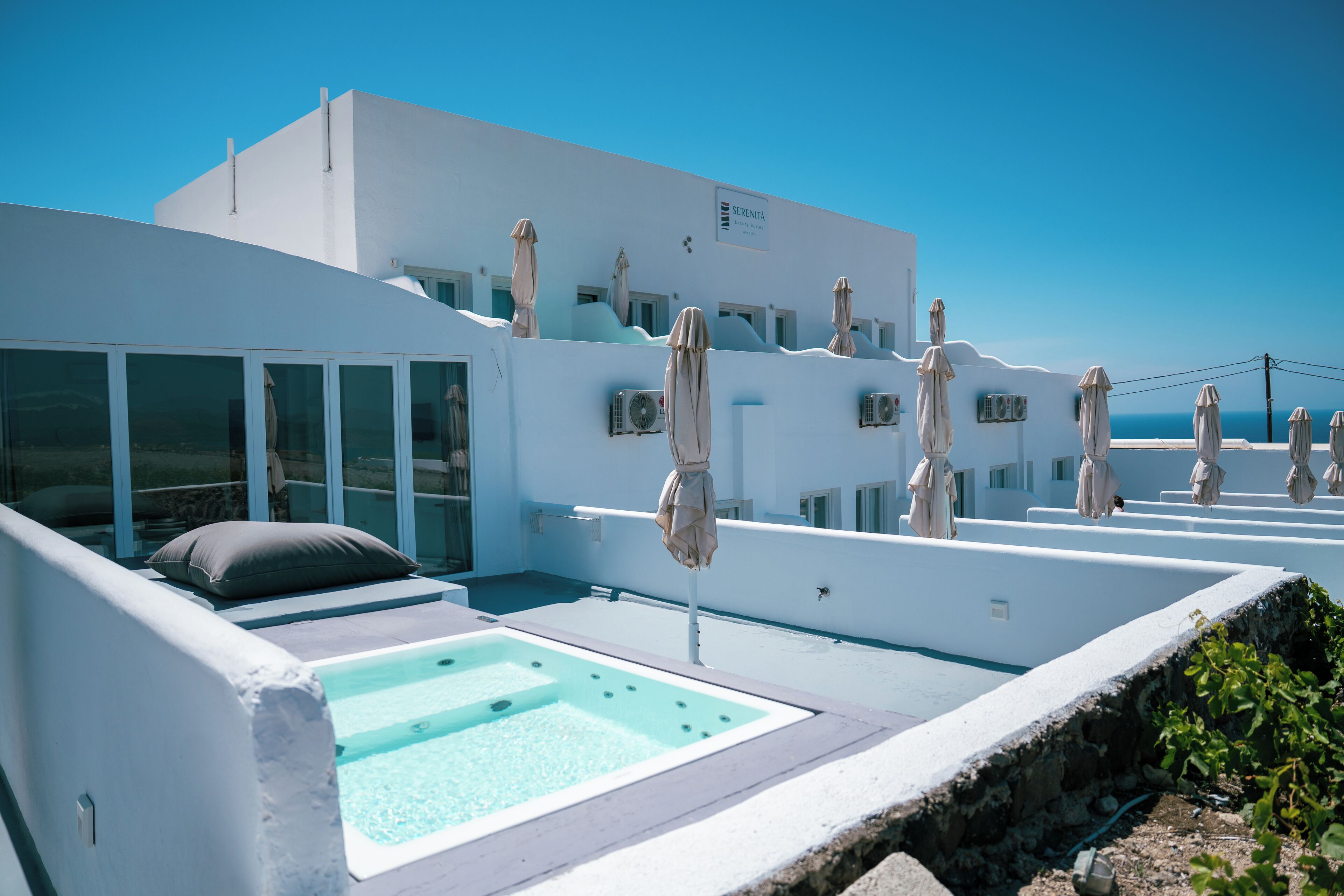 A modern white building with a rooftop pool, outdoor seating, and umbrellas.