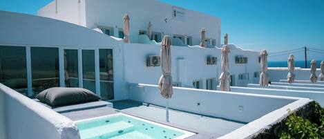 A modern white building with a rooftop pool, outdoor seating, and umbrellas.