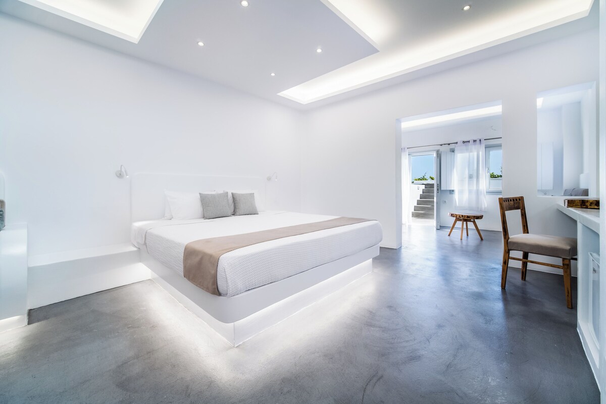 A modern bedroom with a large bed, a wooden chair, and a staircase leading to an outdoor area.