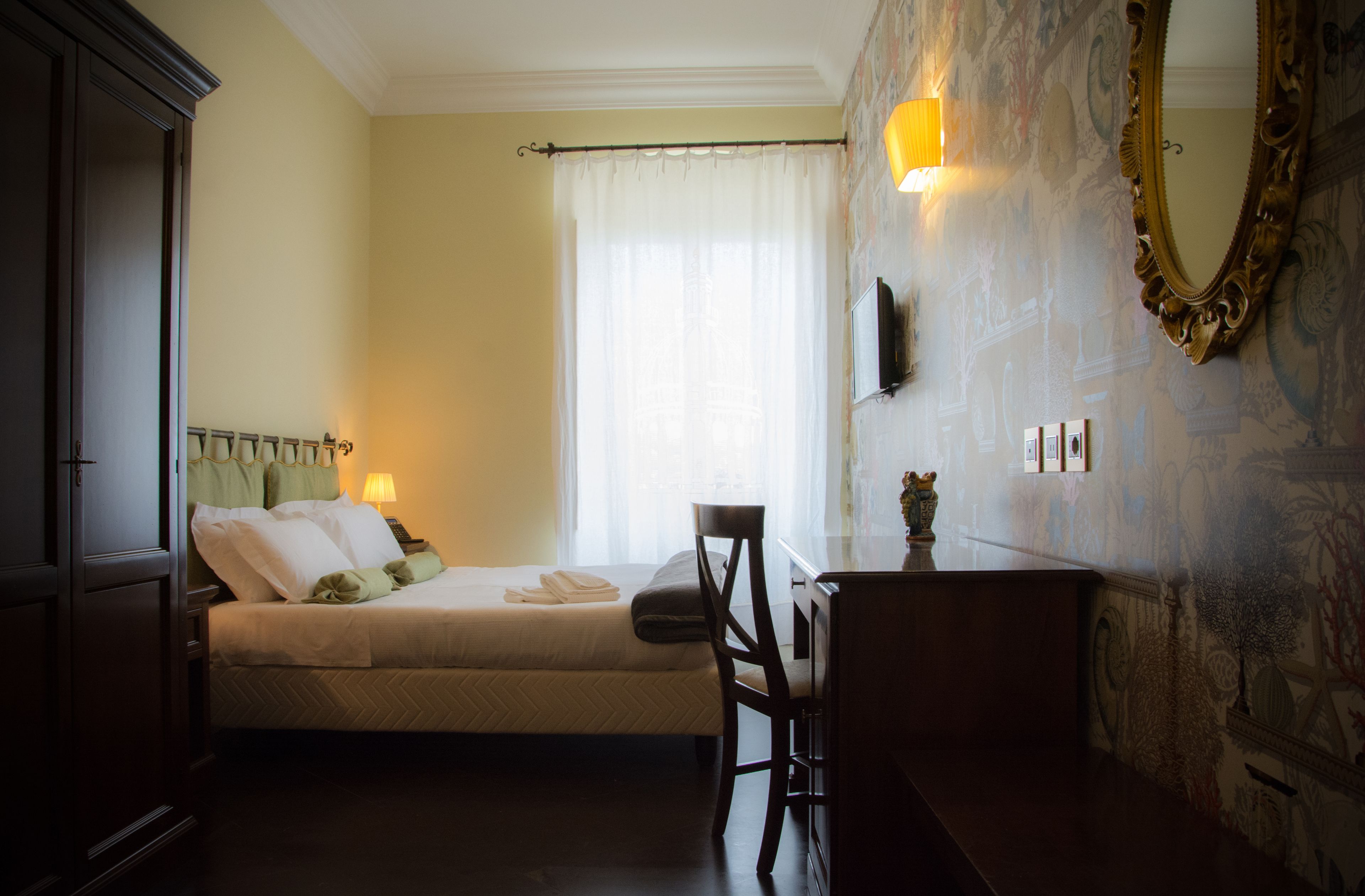 Une chambre d’hôtel comprenant un lit, un bureau, une chaise, une armoire et un grand miroir.