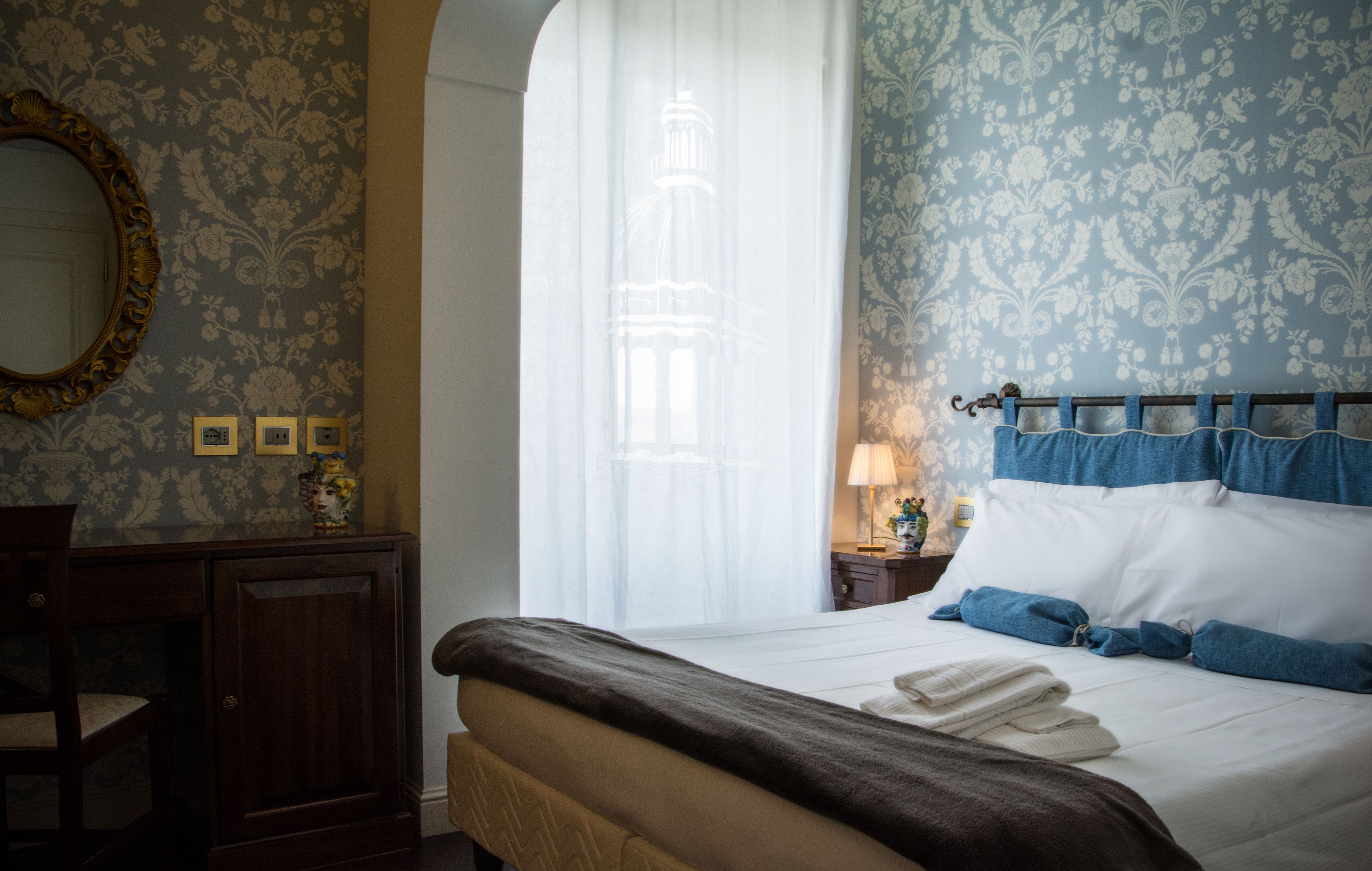 Ein Hotelzimmer mit einem Bett, einer Holzkommode, einem Spiegel und einem Fenster mit Vorhängen.
