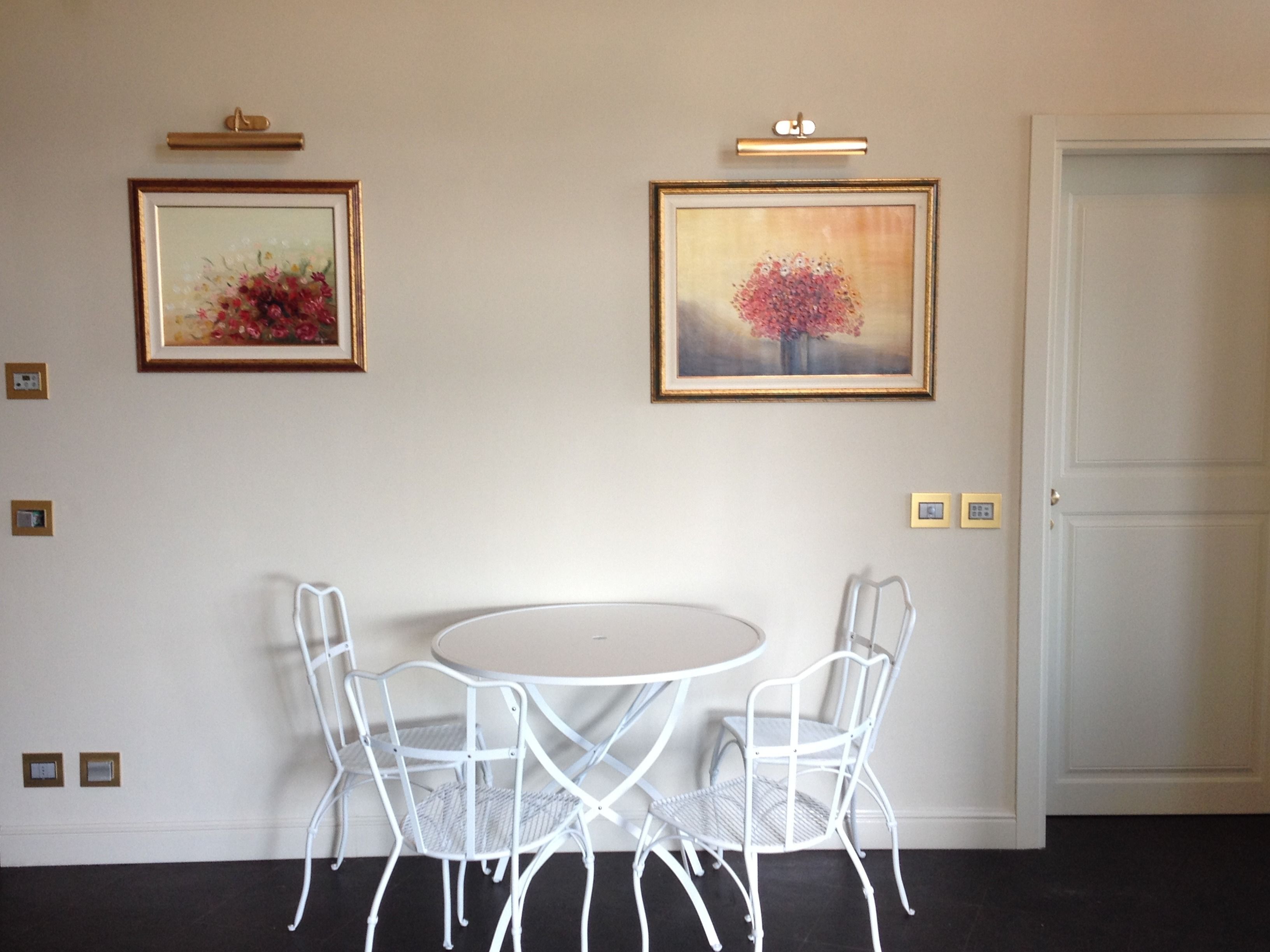 Un coin repas avec une table ronde et quatre chaises blanches, deux tableaux encadrés accrochés au mur et une porte fermée.