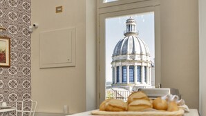 Un buffet per la colazione con croissant e dolci, un tavolo bianco e vista su un edificio con una cupola attraverso una finestra.