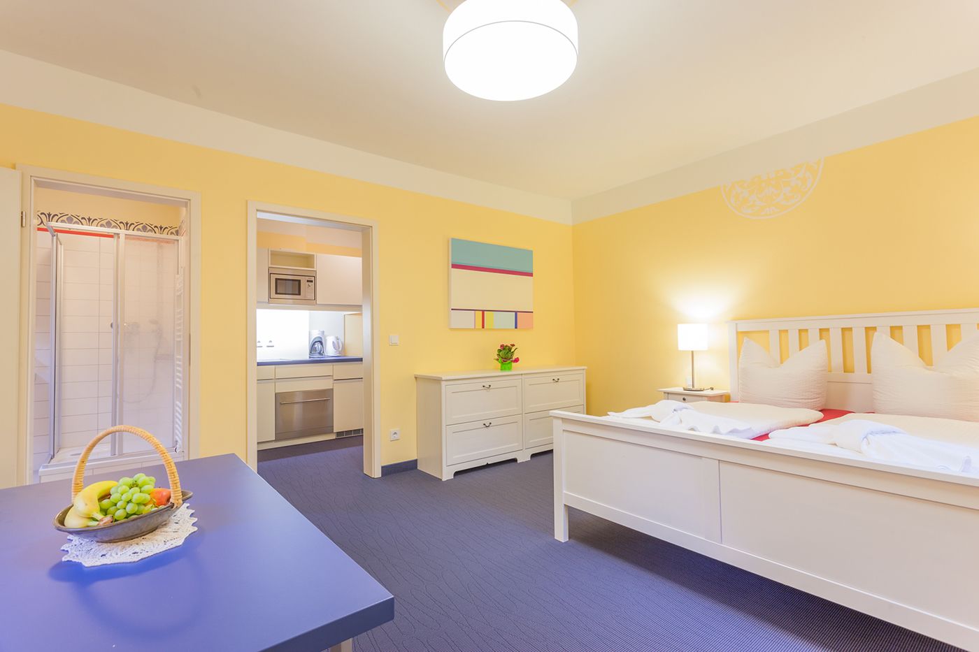 Een hotelkamer met een bed, nachtkastje en een kleine kitchenette.