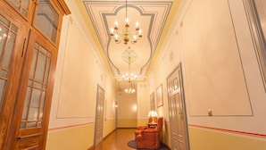 Un pasillo con puertas de madera, un candelabro y un sillón estampado.