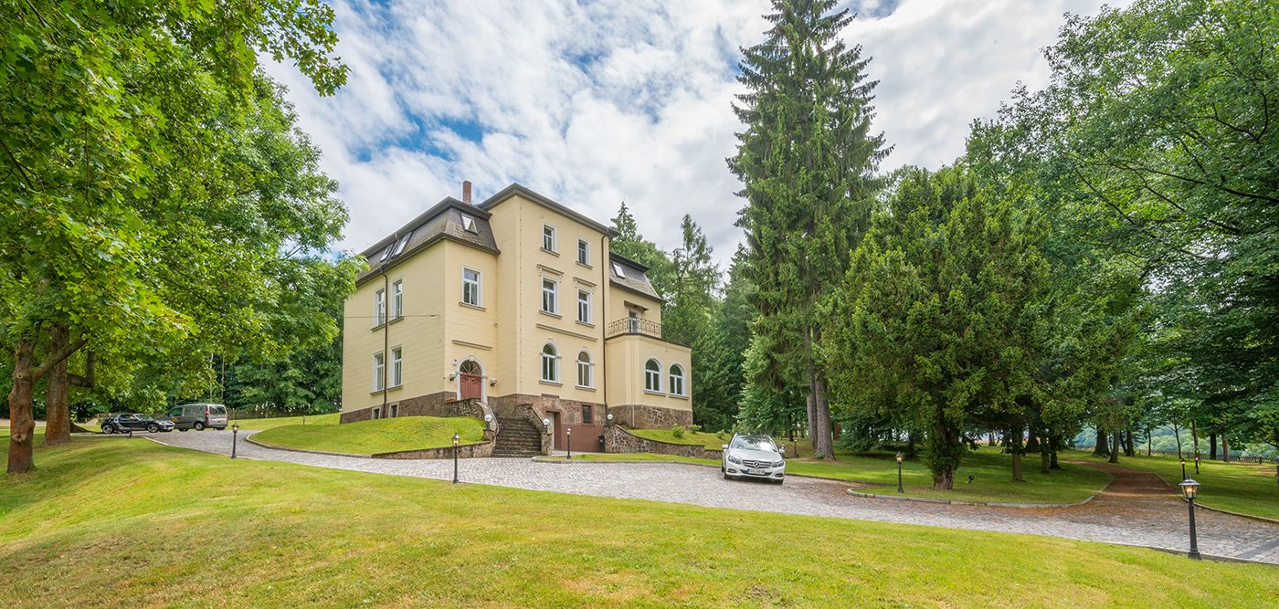 A large, multi-story building with a symmetrical facade, surrounded by lush greenery and trees.
