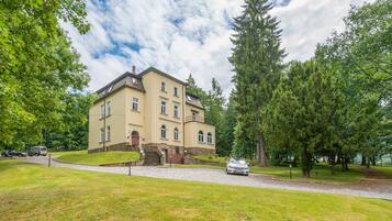 A large, multi-story building with a symmetrical facade, surrounded by lush greenery and trees.
