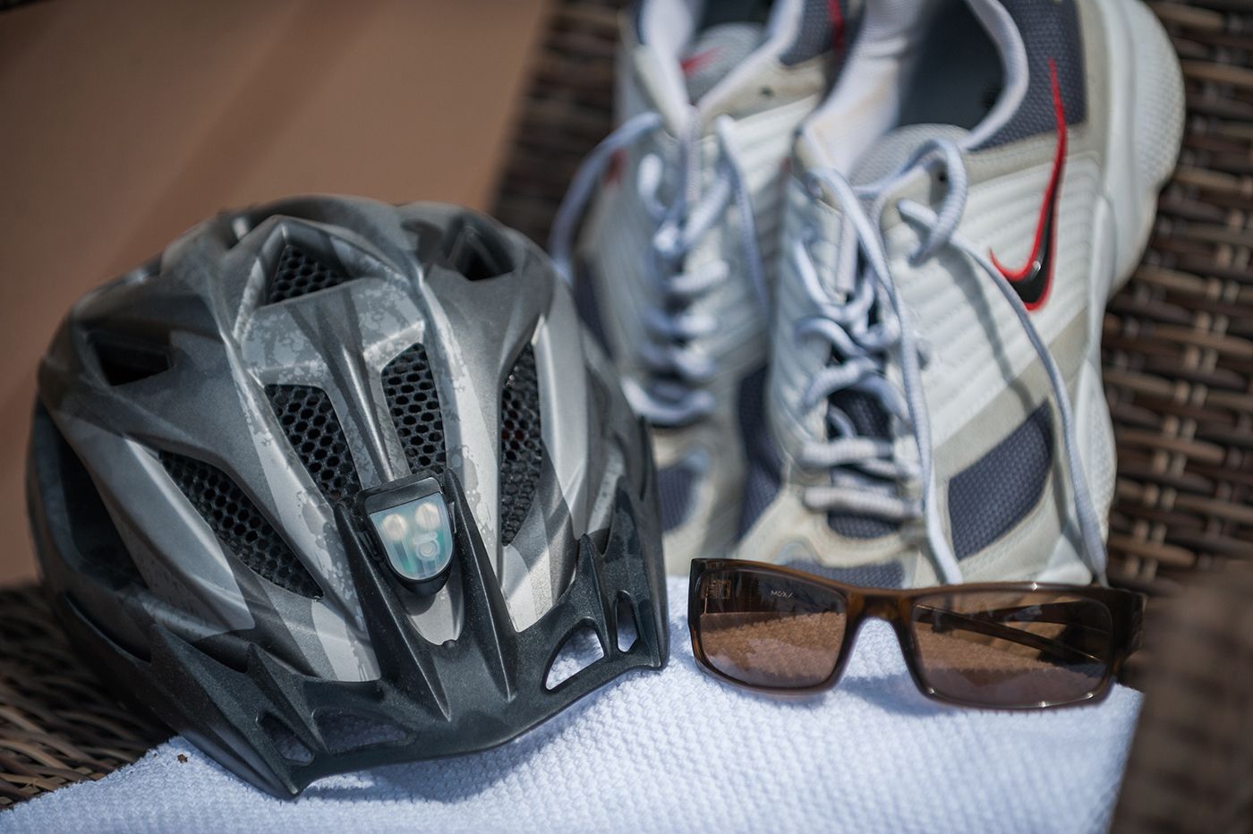 A bicycle helmet, a pair of sneakers, and sunglasses on a white towel.