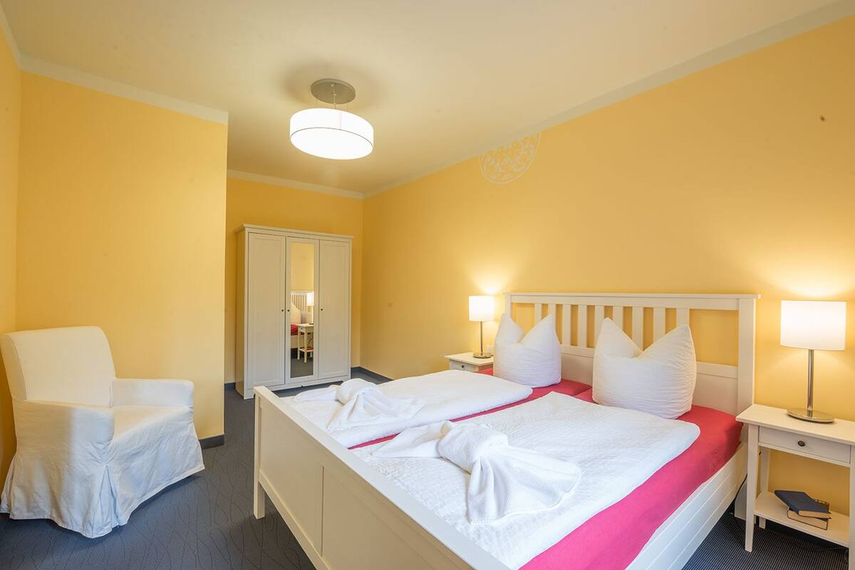 A hotel room with a bed, a chair, a wardrobe, and a desk.