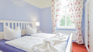A bedroom with two beds, a window with floral curtains, and a white headboard.