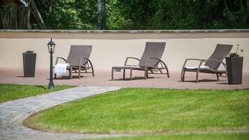 Eine Terrasse mit drei Korbsessel-Loungemöbeln, einem Weg und einem Laternenpfosten.