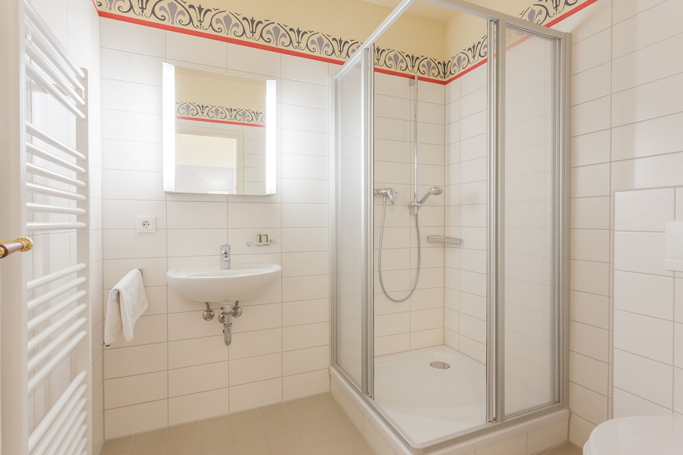 Un baño con ducha de vidrio, un lavamanos con espejo y una toalla colgada en un radiador.
