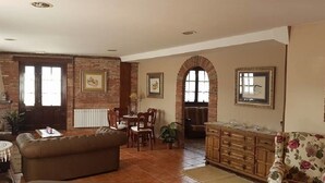 A living room with a brown leather sofa, a dining table with chairs, a wooden cabinet, and a floral armchair. - Posada La Cerrá de San Roque (Santillana del Mar)