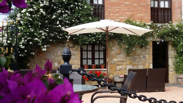 An outdoor patio with a table and chairs, a white umbrella, and potted plants. - Posada La Cerrá de San Roque (Santillana del Mar)