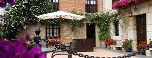Un patio exterior con una mesa y sillas, un paraguas blanco y plantas en macetas.
