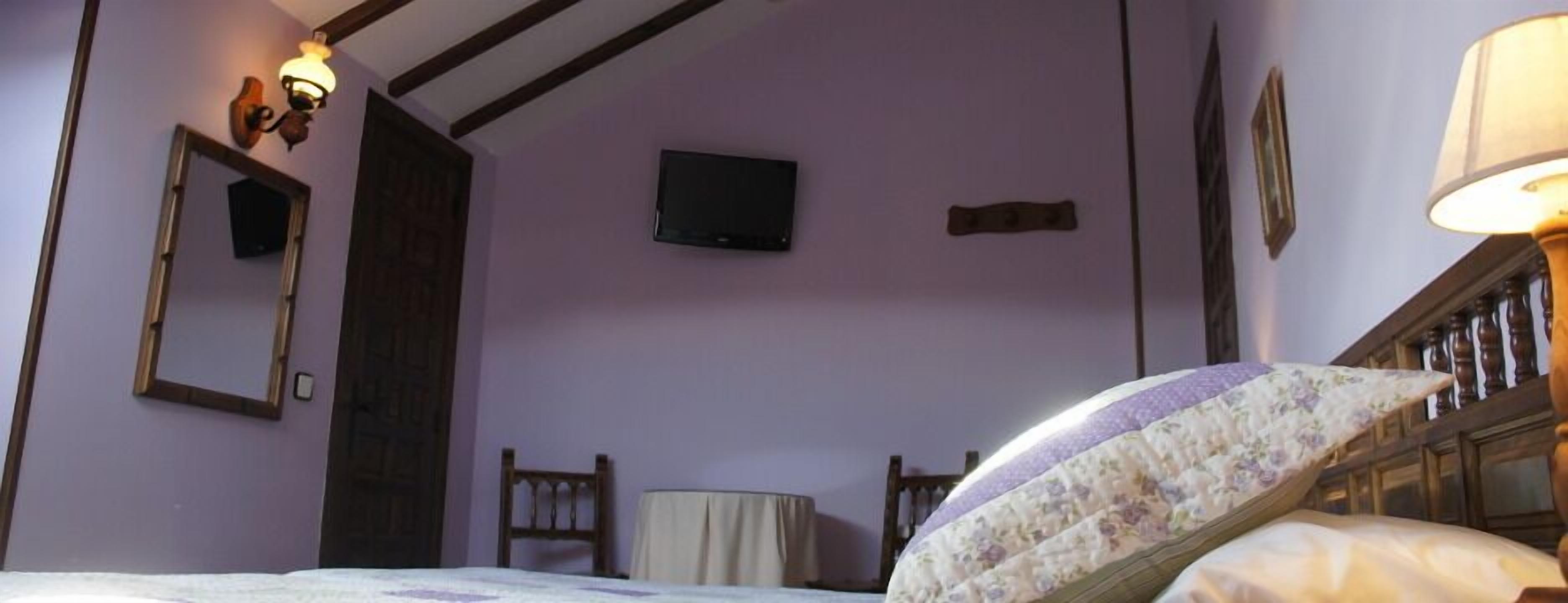 Una habitación con una cama, una silla, una mesita, un televisor y una puerta.