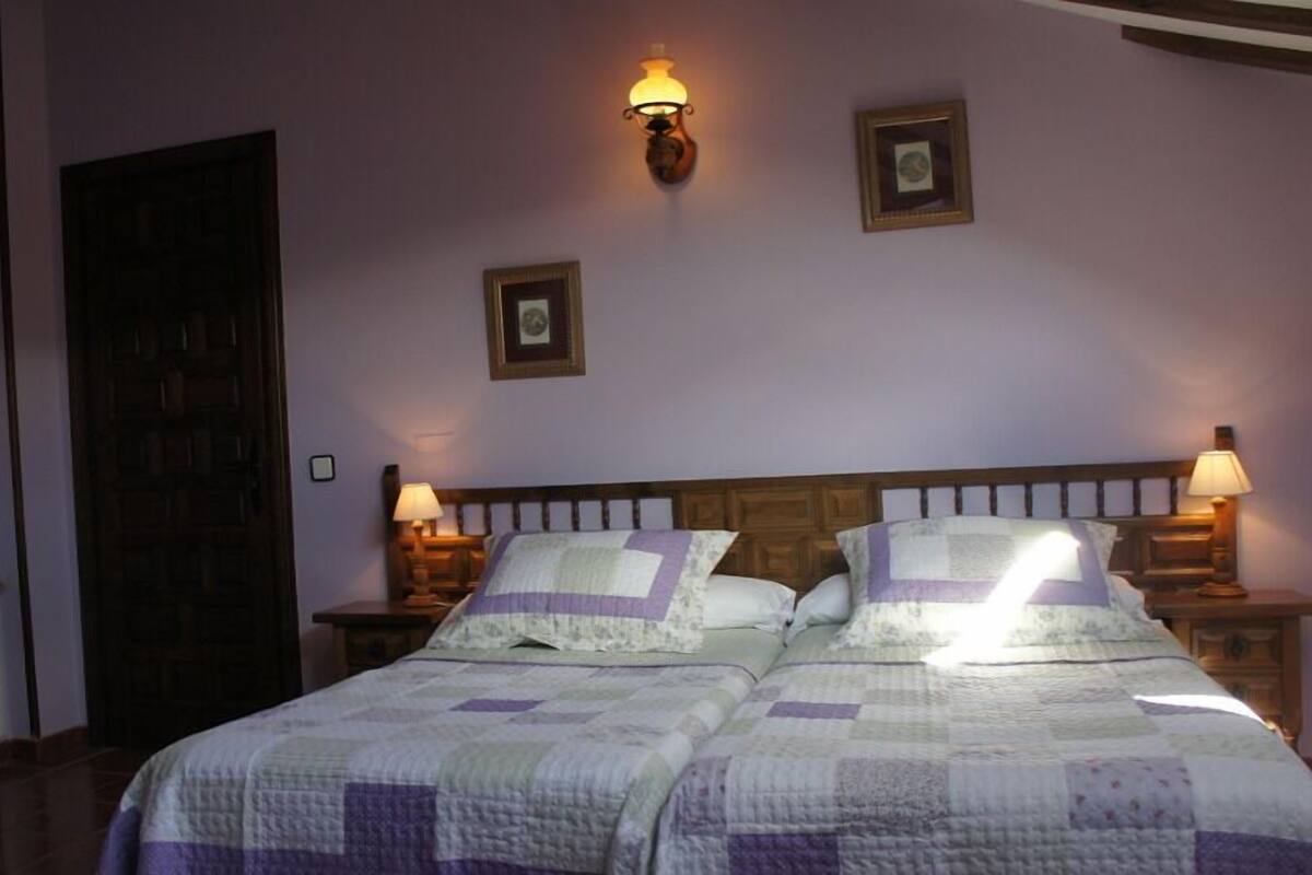 A double bed with a quilt, two bedside lamps, and a wooden headboard.