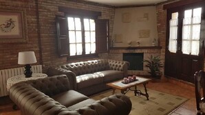 A living room with a leather sofa, a small round table, and a fireplace. - Posada La Cerrá de San Roque (Santillana del Mar)