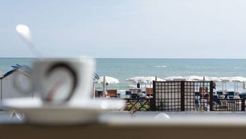 A beachside view with umbrellas and lounge chairs, a gate, and a glimpse of the sea.