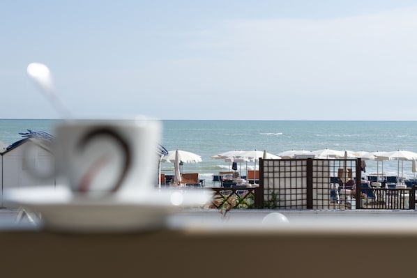 A beachside view with umbrellas and lounge chairs, a gate, and a glimpse of the sea. - Hotel Ambassador (Mondolfo)