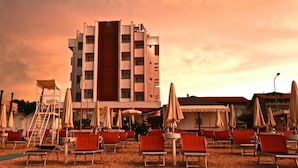 Cet hôtel présente un design moderne, avec une tour centrale et de nombreux balcons. Il dispose d’espaces extérieurs aménagés avec des chaises rouges et des parasols.
