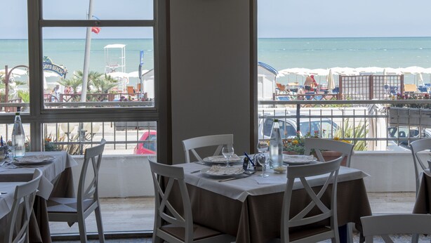 Un restaurant avec des tables dressées pour le service, une vue sur la plage et un poste de surveillance des sauveteurs en arrière-plan.