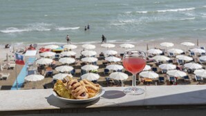 Une vue sur la plage, avec des parasols, une assiette de nourriture et une boisson sur un balcon.
