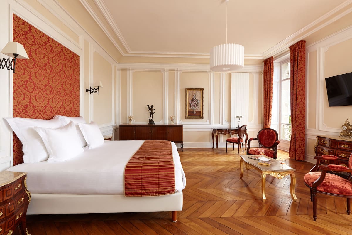 Una habitació d'hotel amb un llit gran, una taula de treball, dues cadires, una televisió i un penjallum.