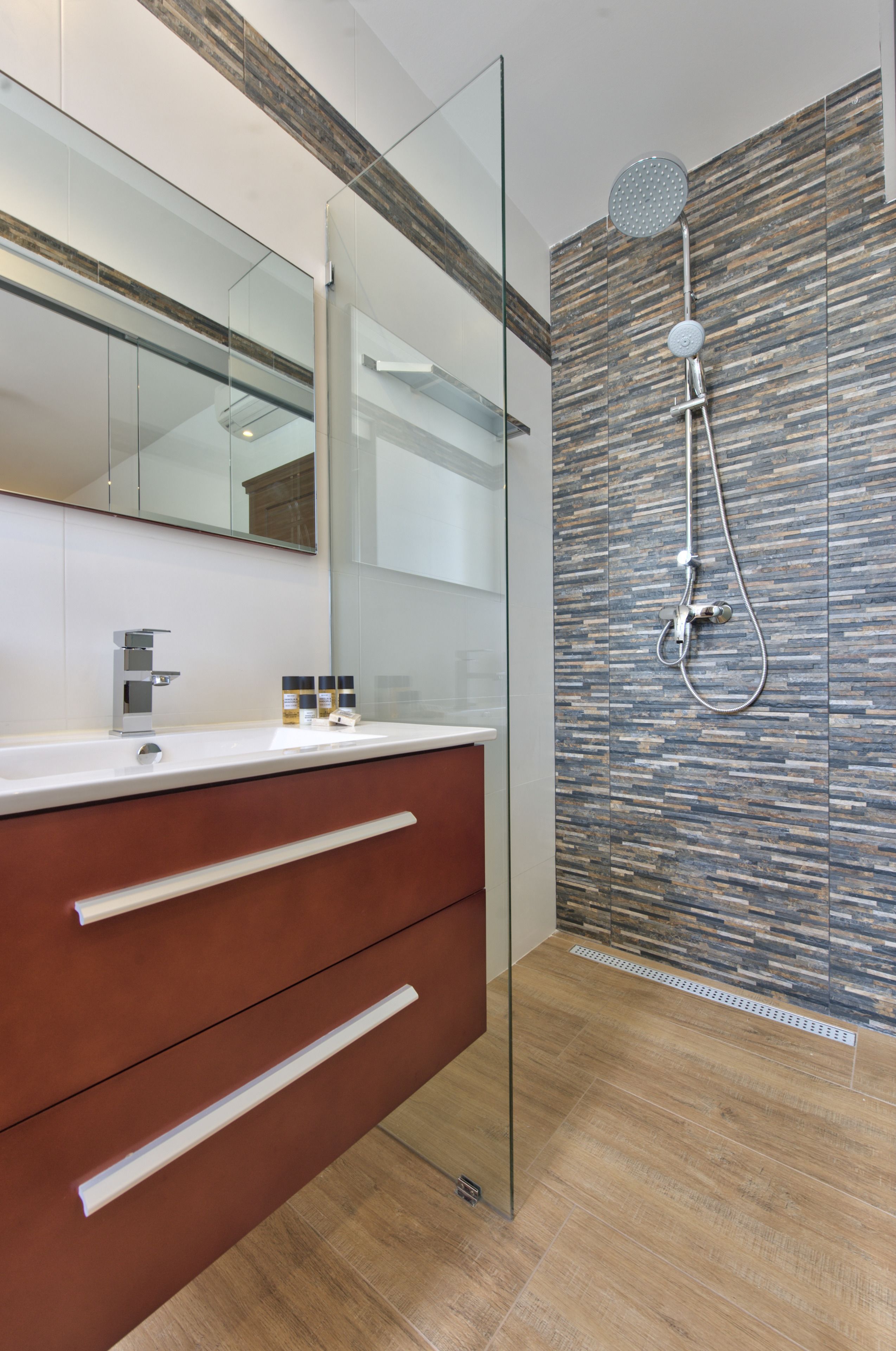 A modern bathroom with a glass shower enclosure, a wooden floor, and a large mirror above the vanity.
