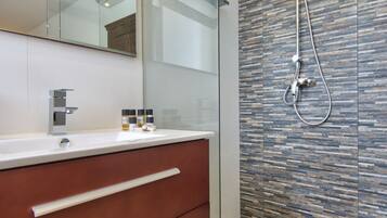 A modern bathroom with a glass shower enclosure, a wooden floor, and a large mirror above the vanity.