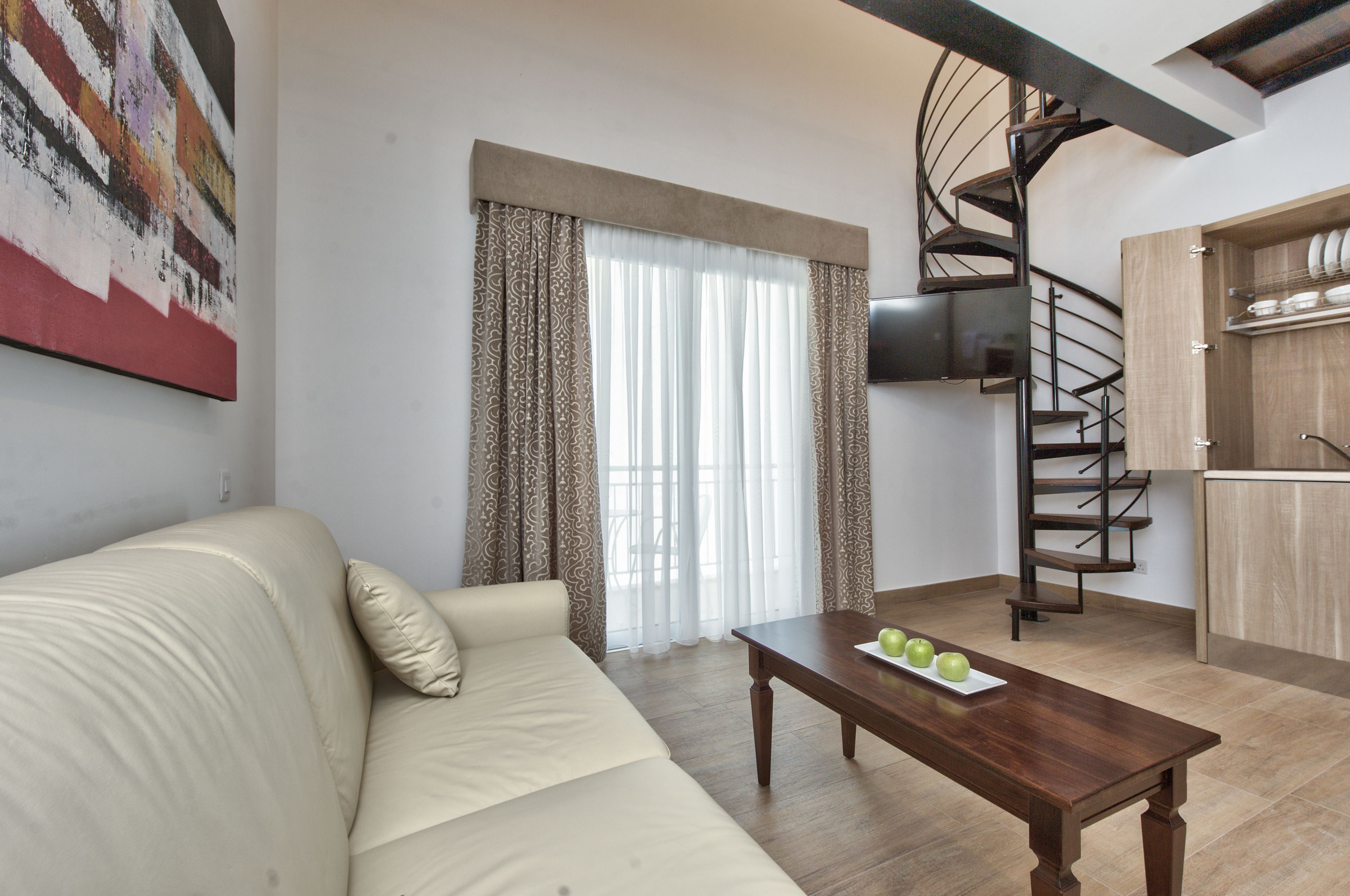 Una sala de estar con sofá, una mesa de centro con manzanas, una escalera en espiral y una zona de cocina.