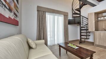 Una sala de estar con sofá, una mesa de centro con manzanas, una escalera en espiral y una zona de cocina.