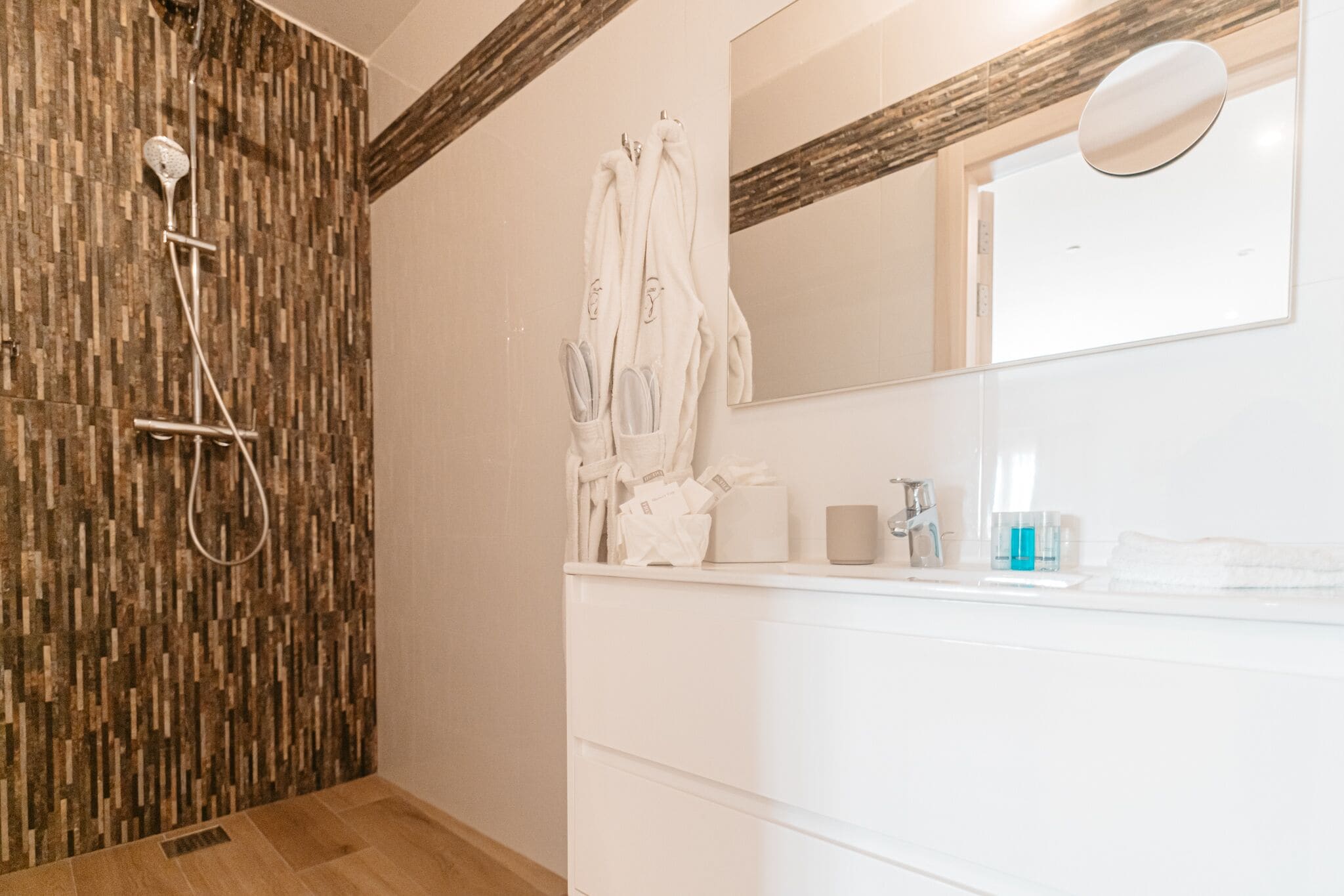 Un baño con pared de ducha de madera, espejo, lavabo con artículos de aseo y toallero.
