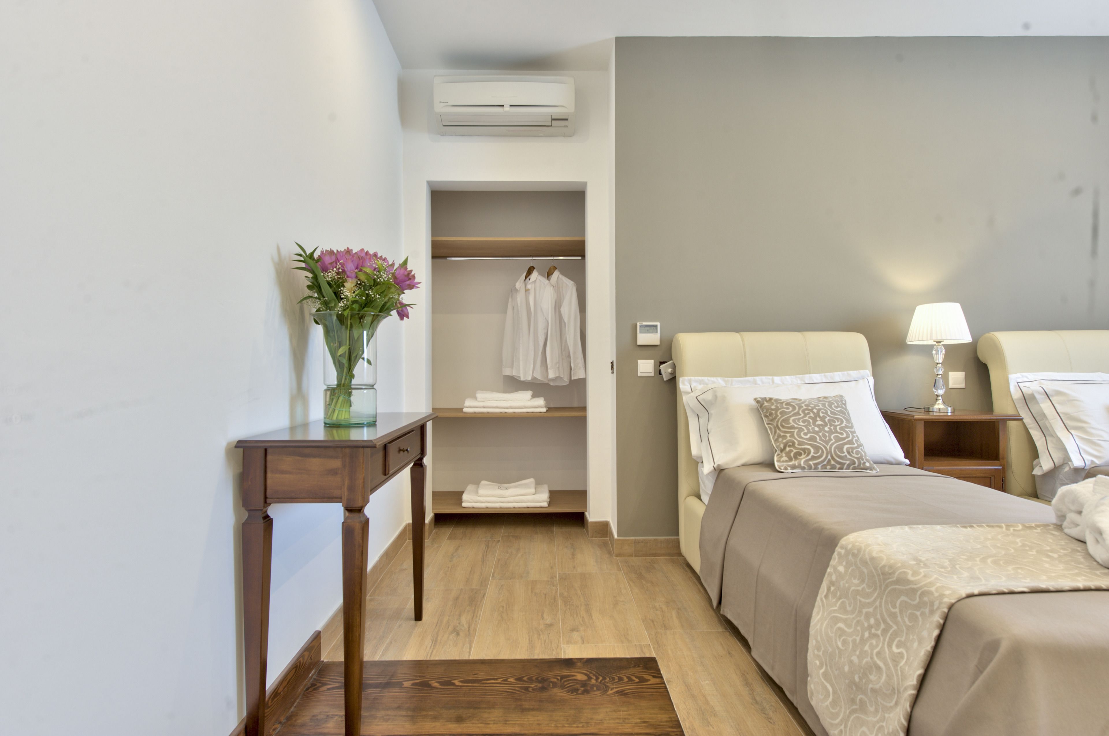 Habitación de hotel con cama, mesitas de noche, escritorio, armario y un florero.