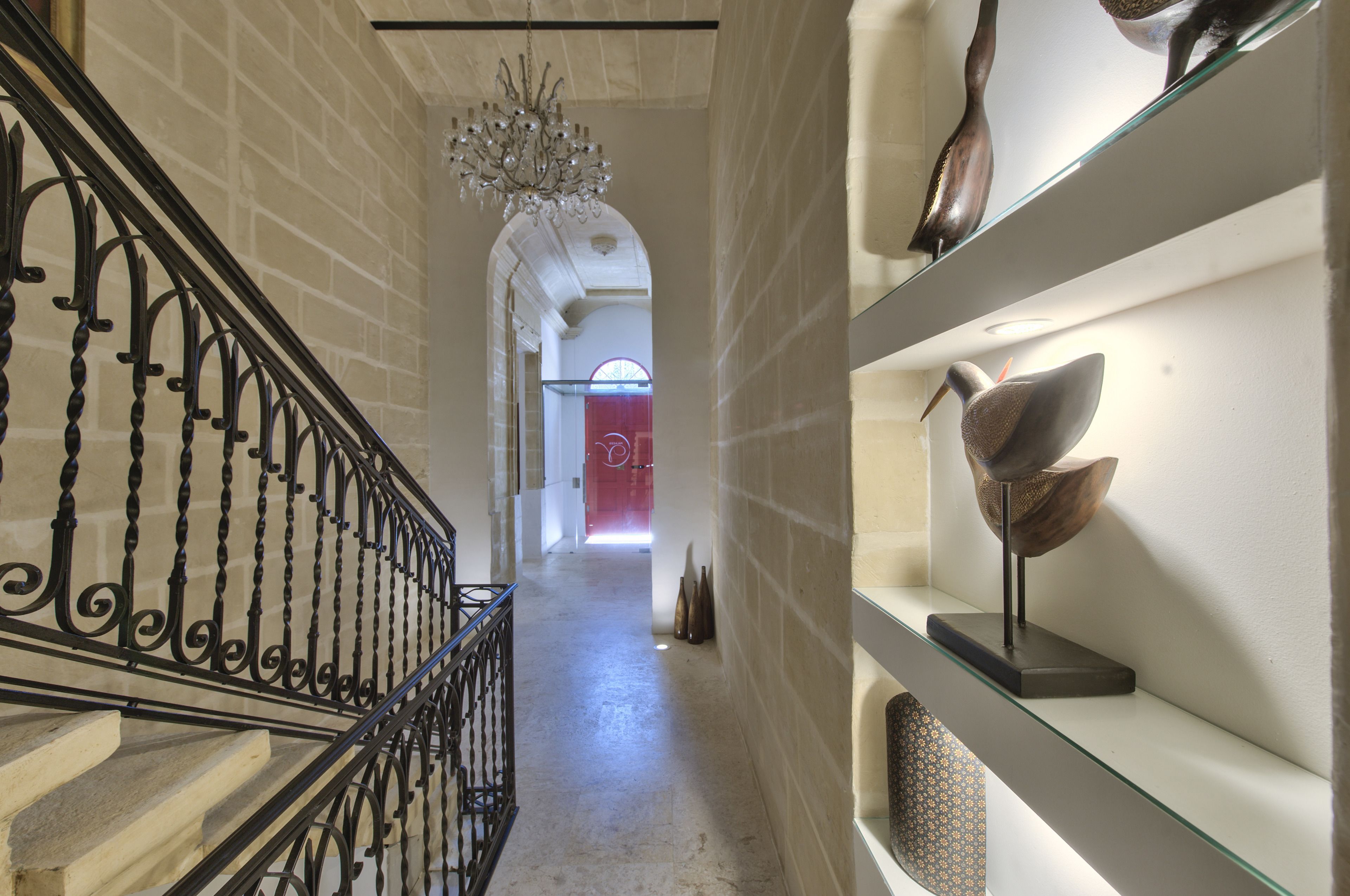 A hallway with a staircase, a chandelier, and shelves with decorative items.