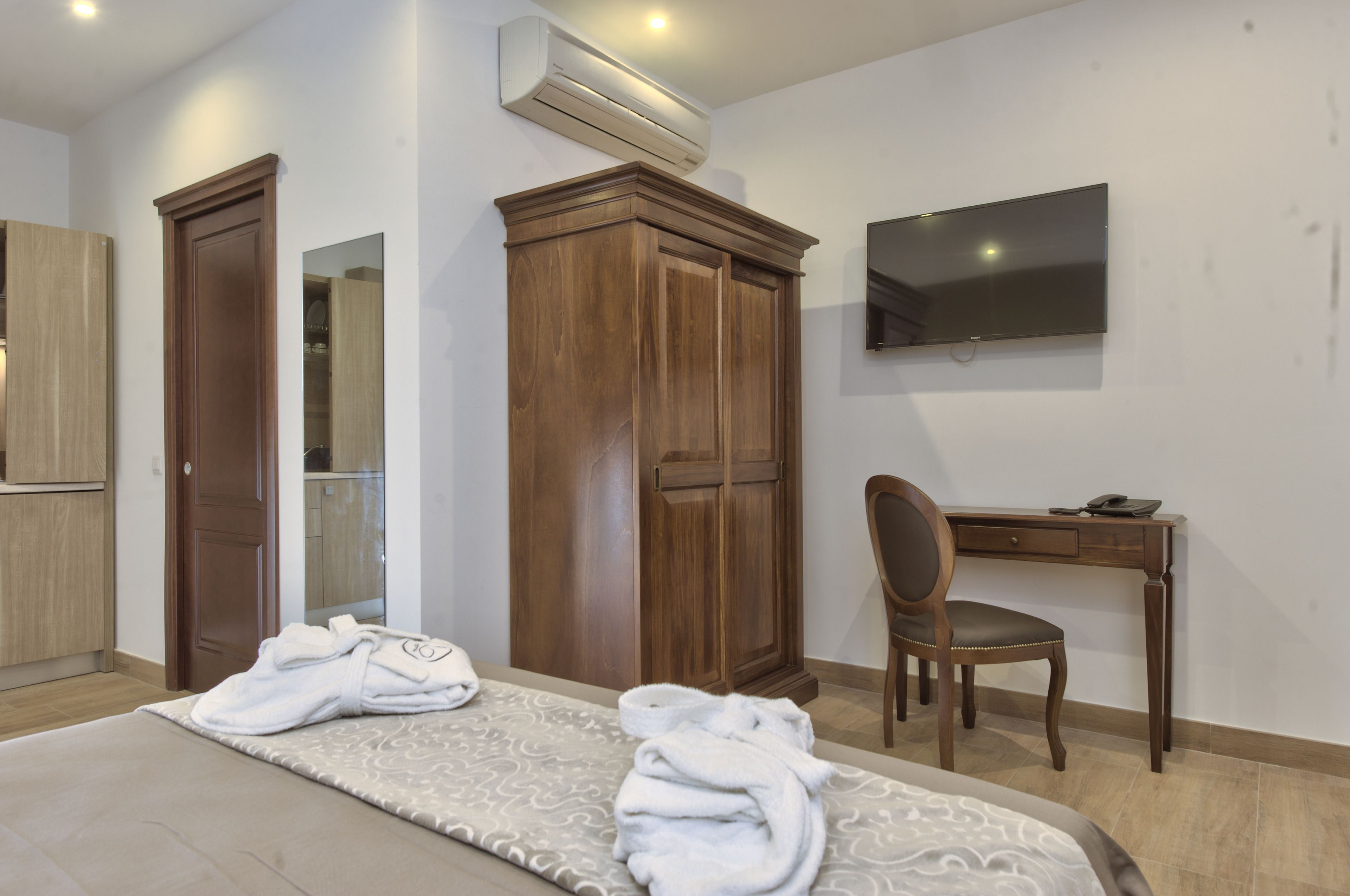 A hotel room with a bed, a desk, a chair, a wardrobe, and a TV mounted on the wall.