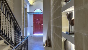 A hallway with a chandelier, a red door, and shelves with decorative items. - Palazzo Violetta (Sliema)