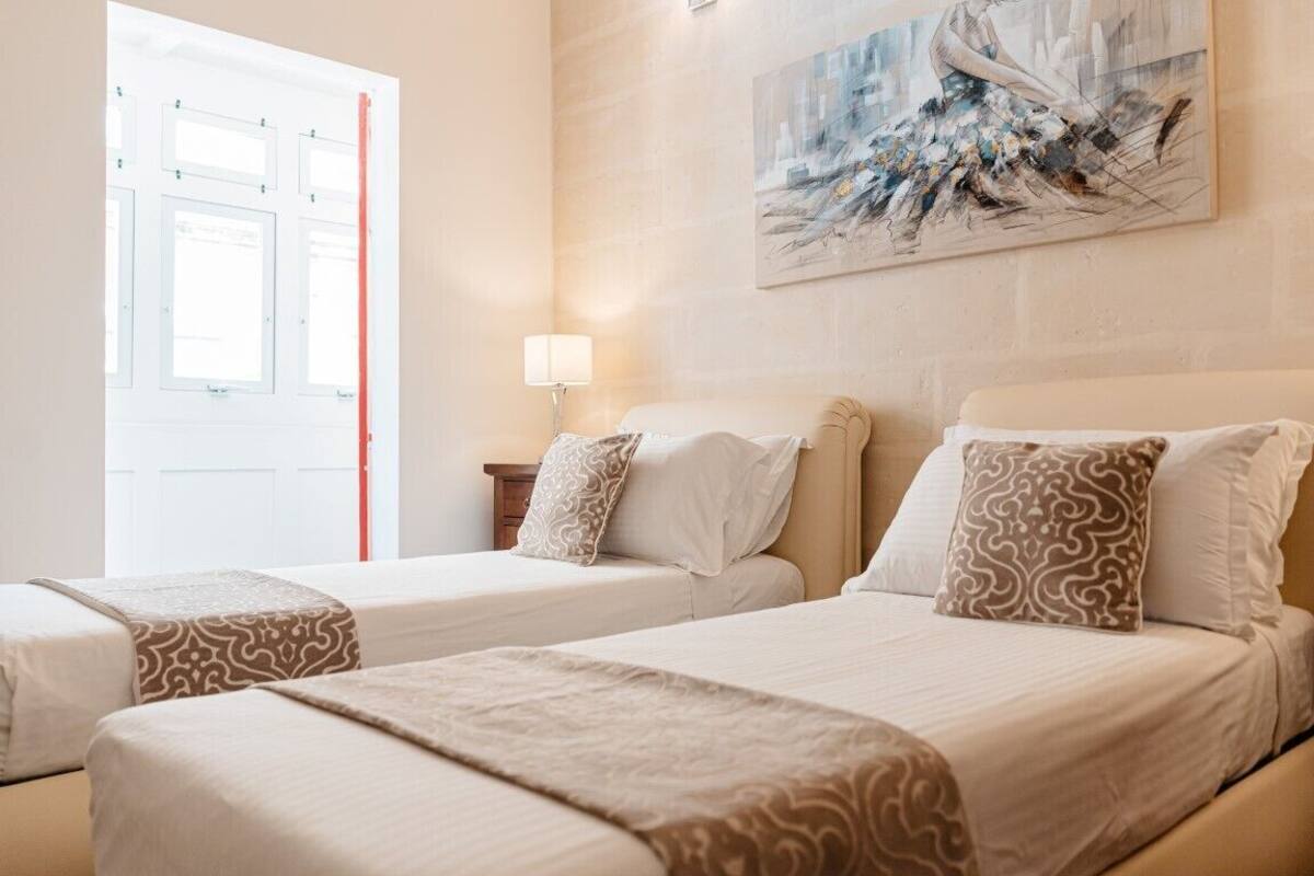 Habitación de hotel con dos camas, un cuadro en la pared, una lámpara y una ventana con persianas.