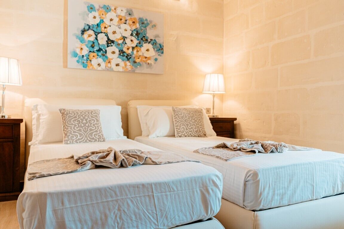 Una camera d'albergo con due letti, un quadro floreale al muro e lampade sui comodini.