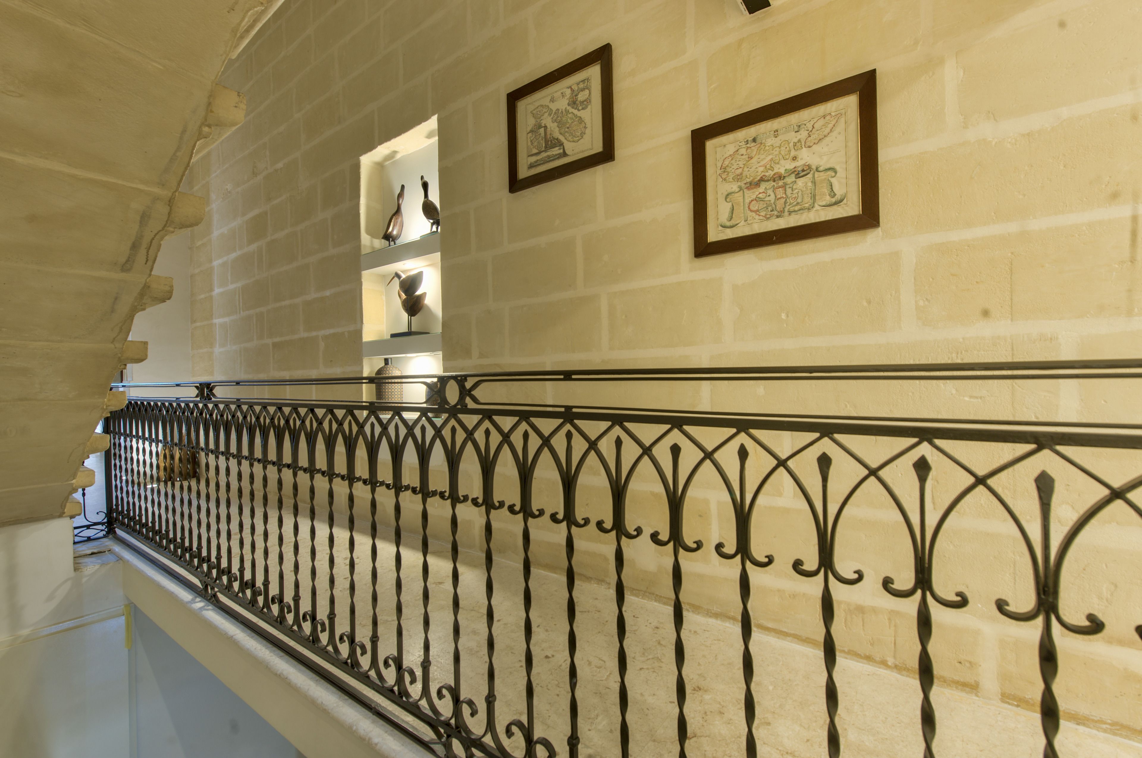 A staircase with a wrought iron railing, a brick wall, and framed artwork.