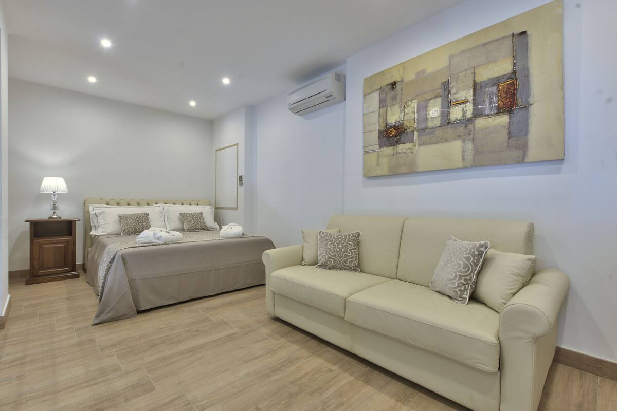 Un dormitorio con cama, sofá, mesita de noche y aire acondicionado instalado en la pared.