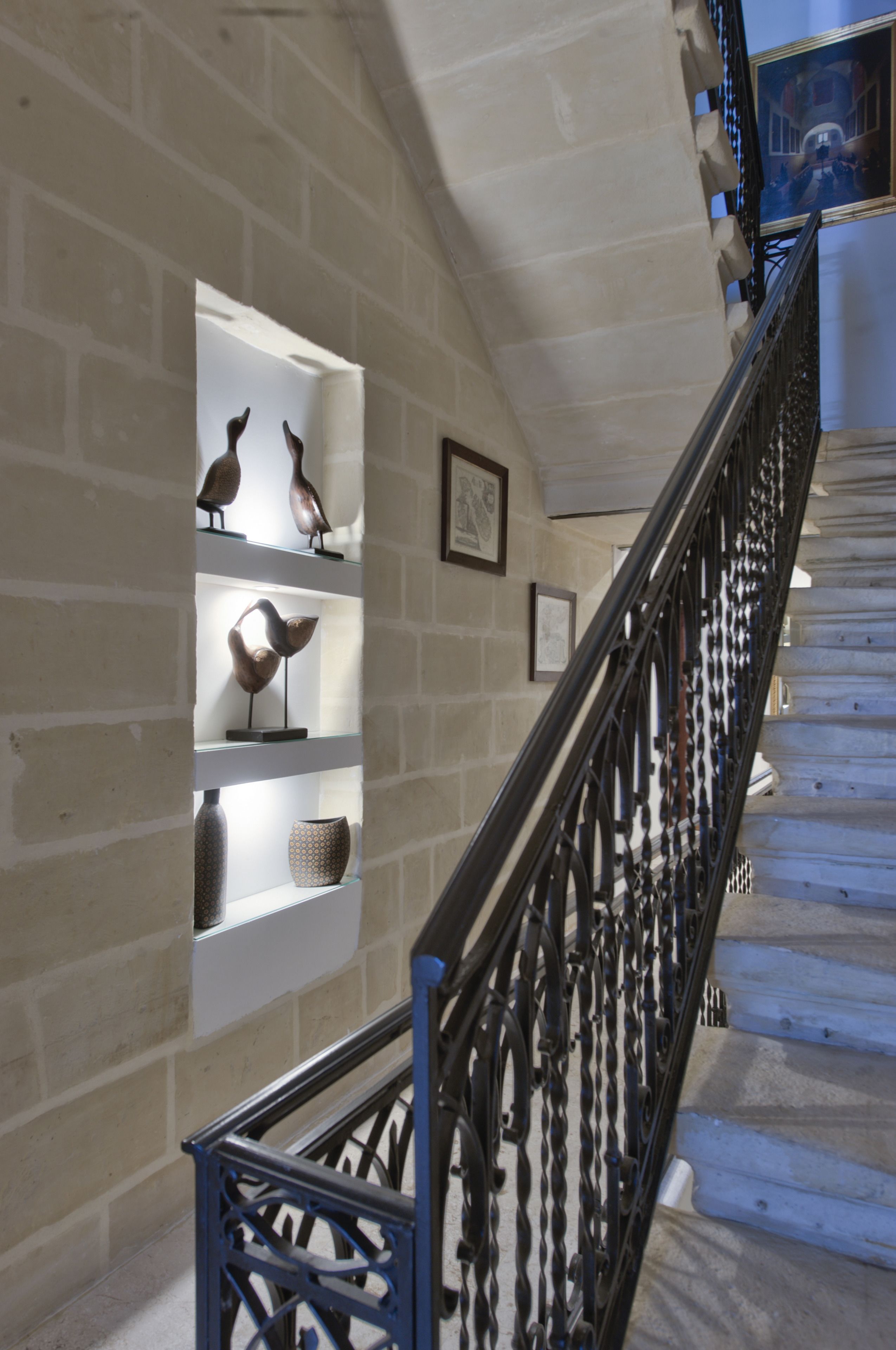 Una escalera con barandilla de metal negro y una pared con estantes que exhiben esculturas de pájaros.