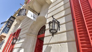 A building facade with red shutters, a sign reading "Ducato," and a wrought iron lantern. - Palazzo Violetta (Sliema)
