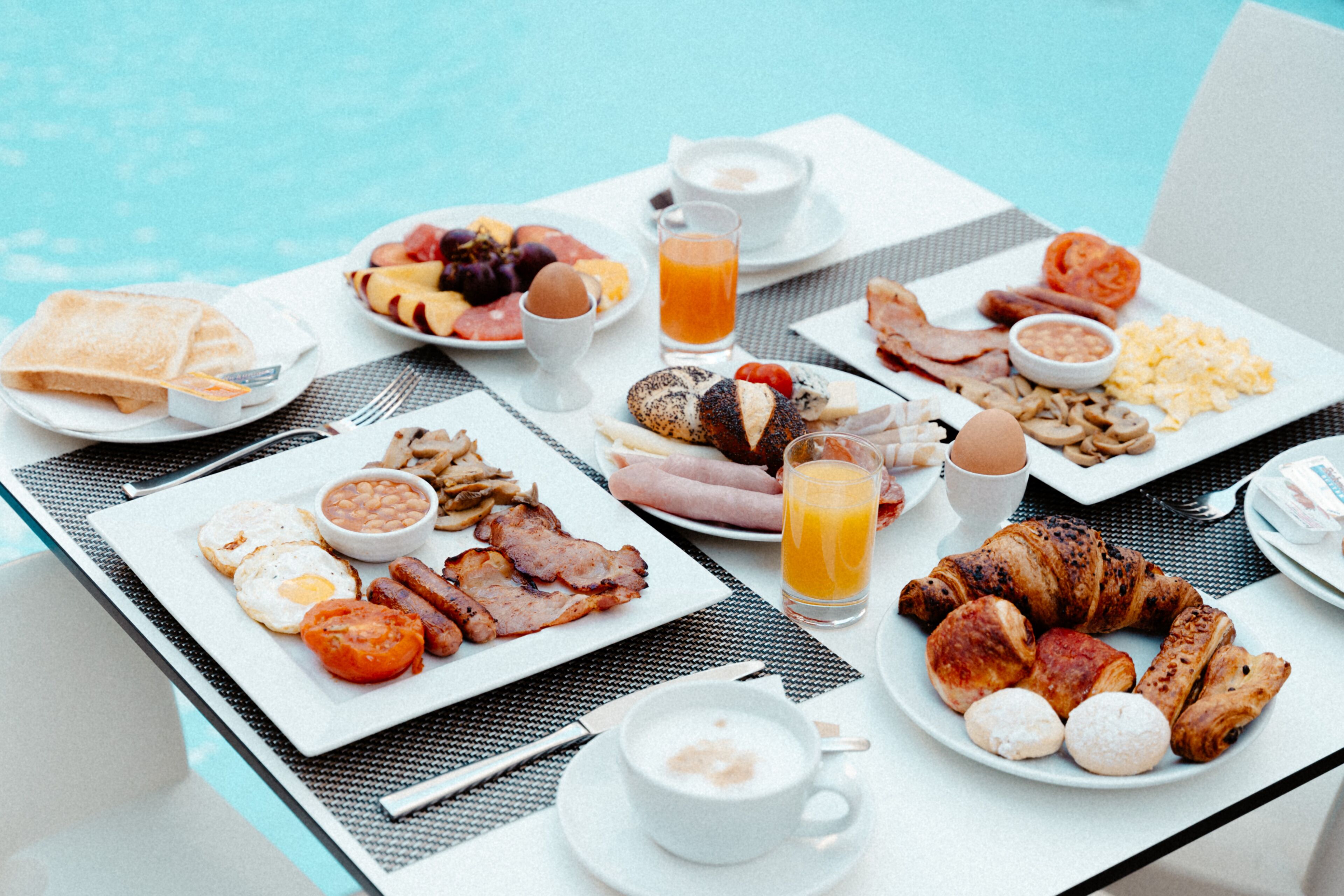 Ein reichhaltiges Frühstücksbuffet mit Speisen und Getränken an einem Tisch neben einem Pool.