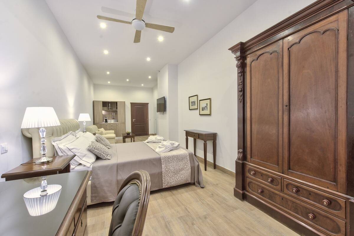 Una habitación de hotel con cama, mesita de noche, lámpara, armario y ventilador de techo.
