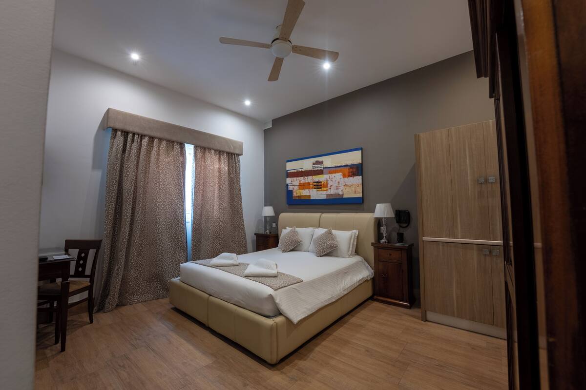 Un dormitorio con una cama, un escritorio, una silla, un armario y un ventilador de techo.