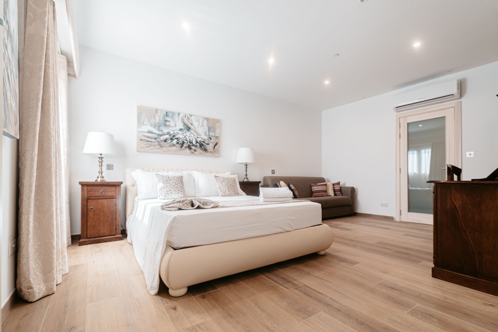 Ein Schlafzimmer mit einem großen Bett, zwei Nachttischen mit Lampen, einem Sofa und Holzboden.
