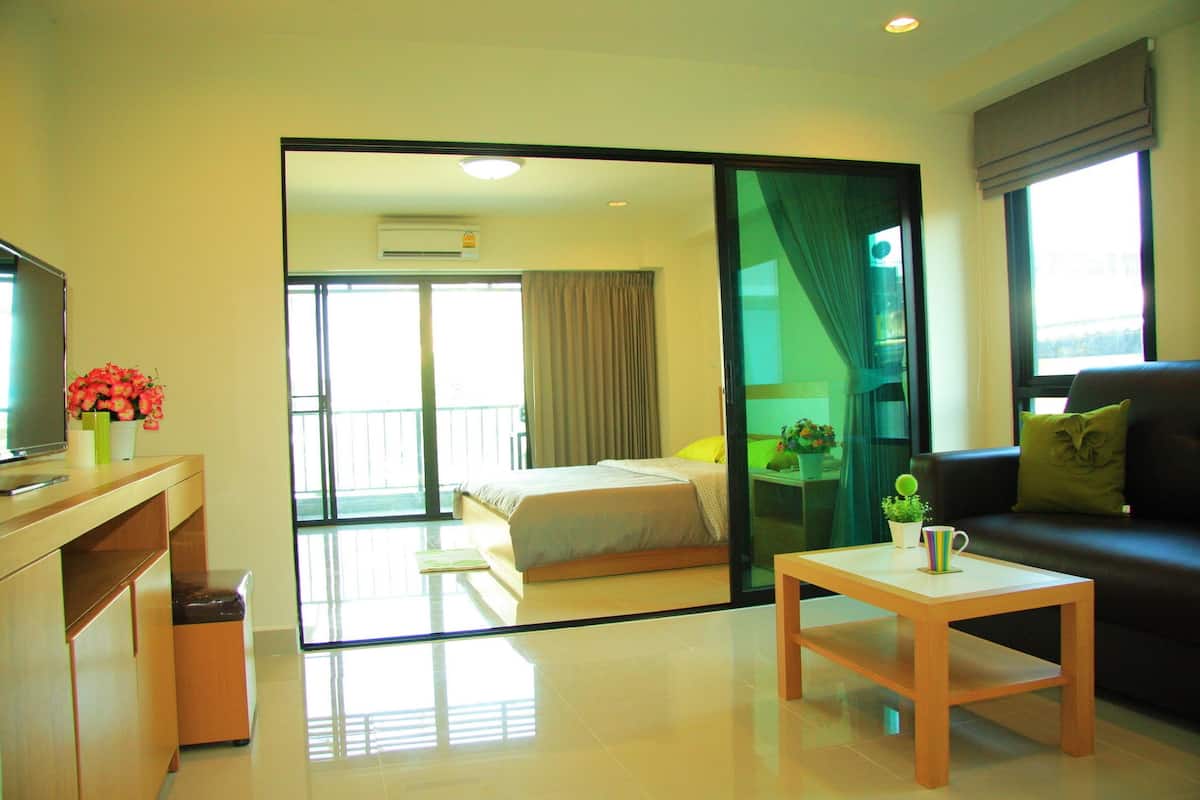 A modern hotel room with a bed, a sofa, a coffee table, and a TV on a wooden cabinet.
